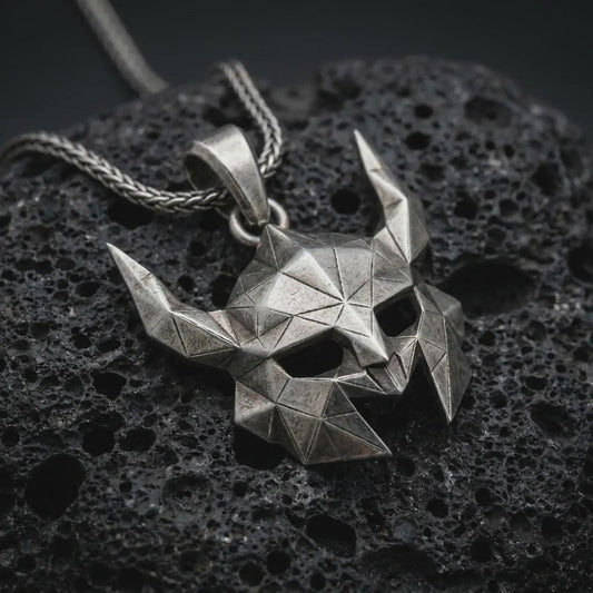 An oxidized Helm of Awe inspired mask pendant rests on dark volcanic rock in a macro studio close-up, showing a faceted horned Norse warrior design.