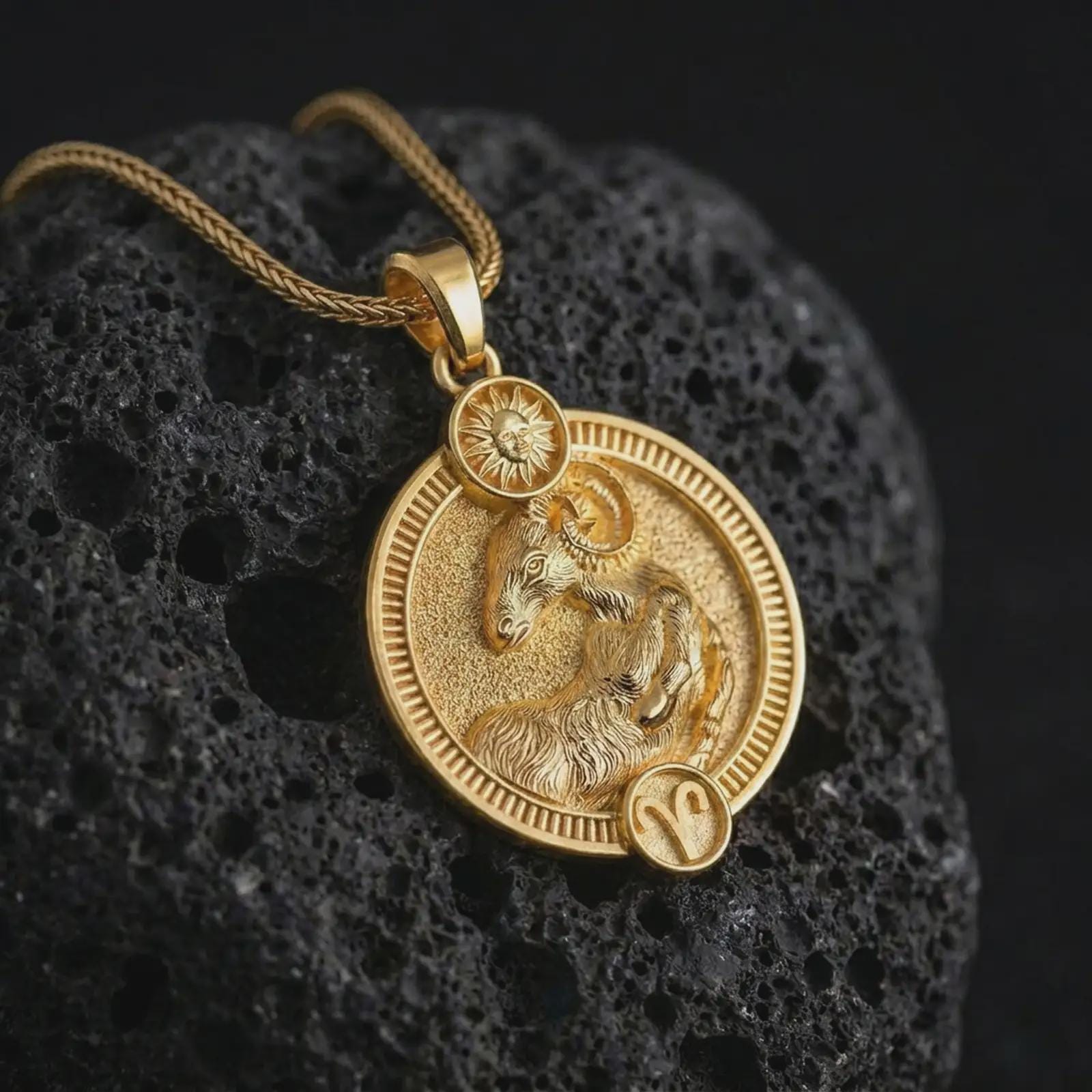 Gold plated Aries zodiac pendant necklace on textured volcanic rock, premium close-up studio composition emphasizing the ram figure, sun motif, and astrology medallion design.
