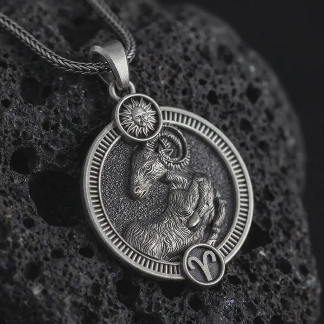 Oxidized Aries zodiac pendant necklace on textured volcanic rock, close-up studio shot highlighting the ram relief, sun detail, Aries symbol, and antique silver contrast.