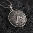 Load image into Gallery viewer, Oxidized Spartan shield pendant necklace on textured volcanic rock, close-up studio shot highlighting the cracked round shield, raised lambda symbol, battle-worn texture, and antique silver contrast.
