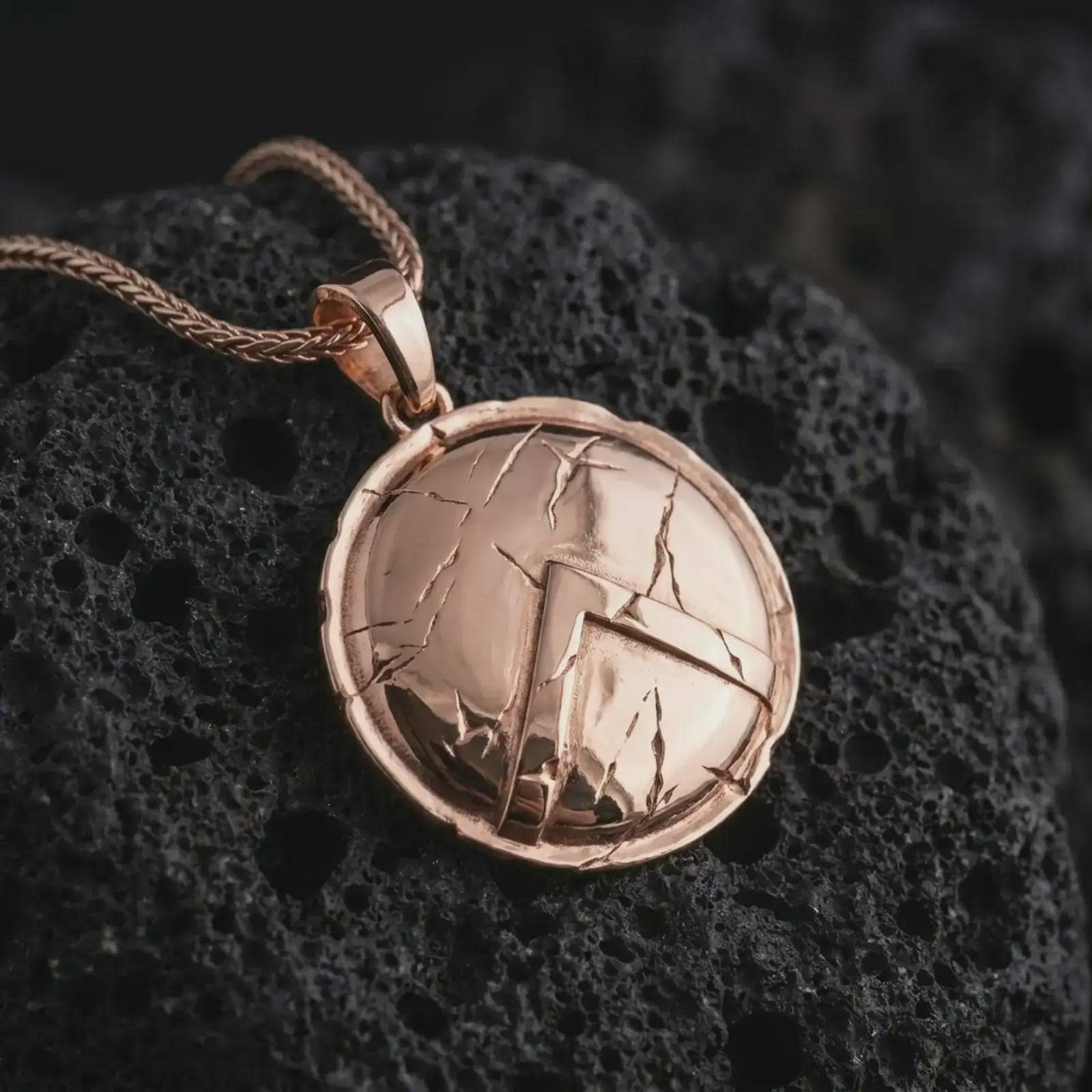 Rose gold plated Spartan shield pendant necklace on textured volcanic rock, detailed macro product shot with soft warm reflections and bold warrior symbolism.