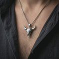 Load image into Gallery viewer, Polished silver bull skull pendant necklace worn on the chest, masculine lifestyle shot highlighting the bright silver finish, long horns, and sculpted skull detail.
