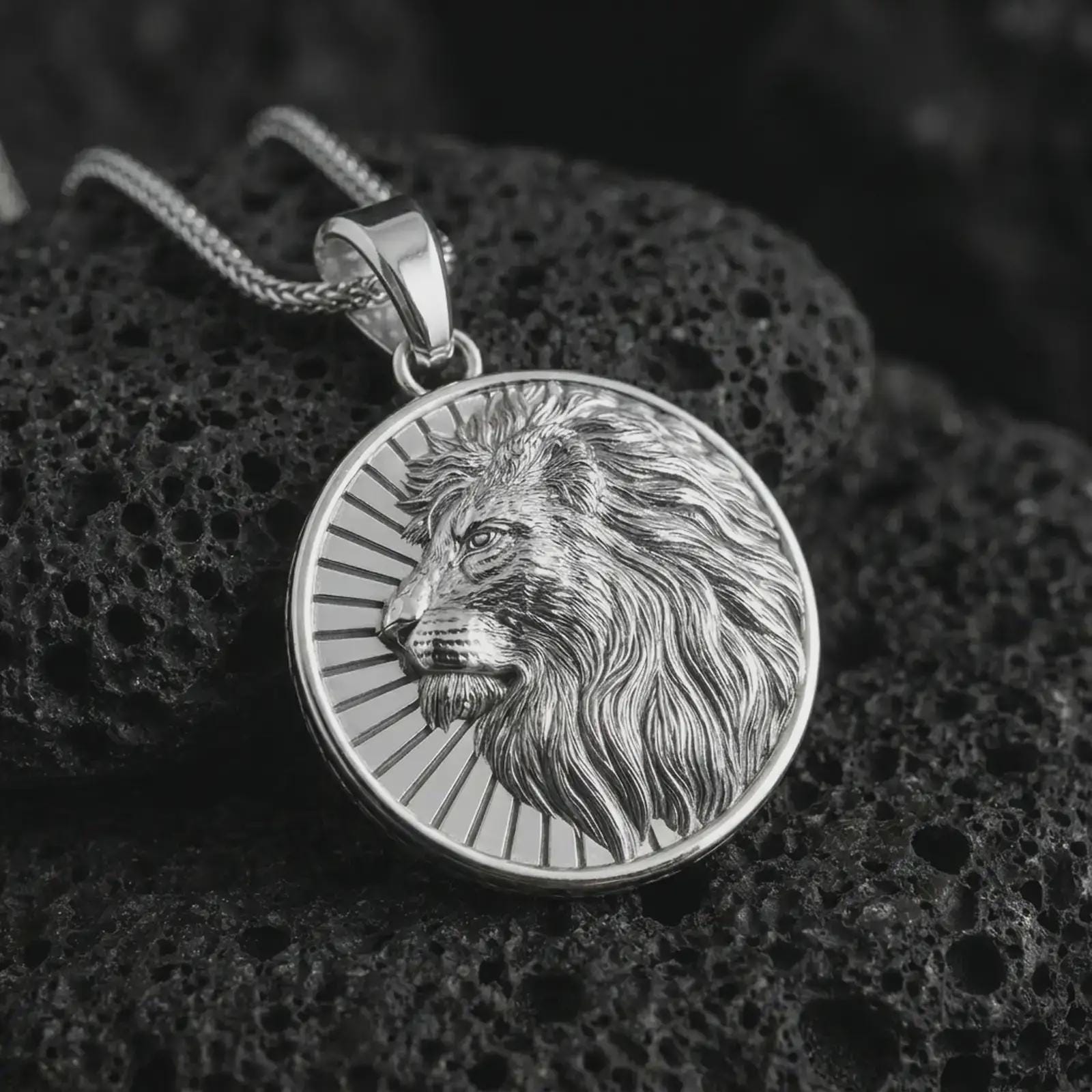Polished silver Lion of Judah pendant necklace on textured volcanic rock, centered macro jewelry photo with detailed lion relief and bright silver highlights.