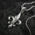 Load image into Gallery viewer, Polished silver fleur-de-lis pendant necklace on textured volcanic rock, centered macro jewelry photo with detailed French Gothic form and bright silver highlights.
