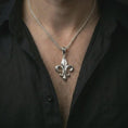 Load image into Gallery viewer, Polished silver fleur-de-lis pendant necklace worn on the chest, masculine lifestyle shot highlighting the bright silver finish, curved lily arms, and sculpted relief.
