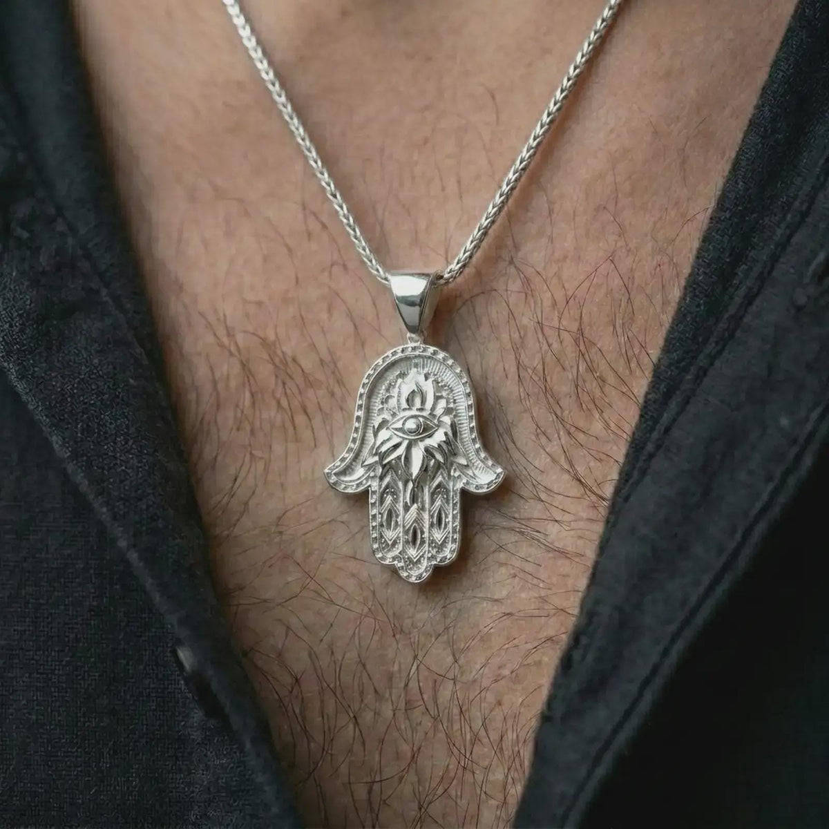 Polished silver hamsa hand pendant necklace worn on the chest, feminine lifestyle shot highlighting the bright silver finish, lotus flower relief, and detailed hand design.