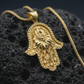 Load image into Gallery viewer, Gold plated hamsa hand pendant necklace on textured volcanic rock, premium close-up studio composition emphasizing the protective hand symbol, lotus details, and spiritual amulet design.
