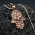 Load image into Gallery viewer, Rose gold plated hamsa hand pendant necklace on textured volcanic rock, detailed macro product shot with soft warm reflections and sacred evil eye symbolism.
