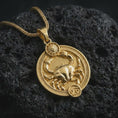 Load image into Gallery viewer, Gold plated Cancer zodiac pendant necklace on textured volcanic rock, premium close-up studio composition emphasizing the crab figure, sun motif, and astrology medallion design.
