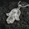 Load image into Gallery viewer, Polished silver hamsa elephant pendant necklace on textured volcanic rock, centered macro jewelry photo with detailed elephant trunk, tusks, spiritual eye motif, and bright silver highlights.
