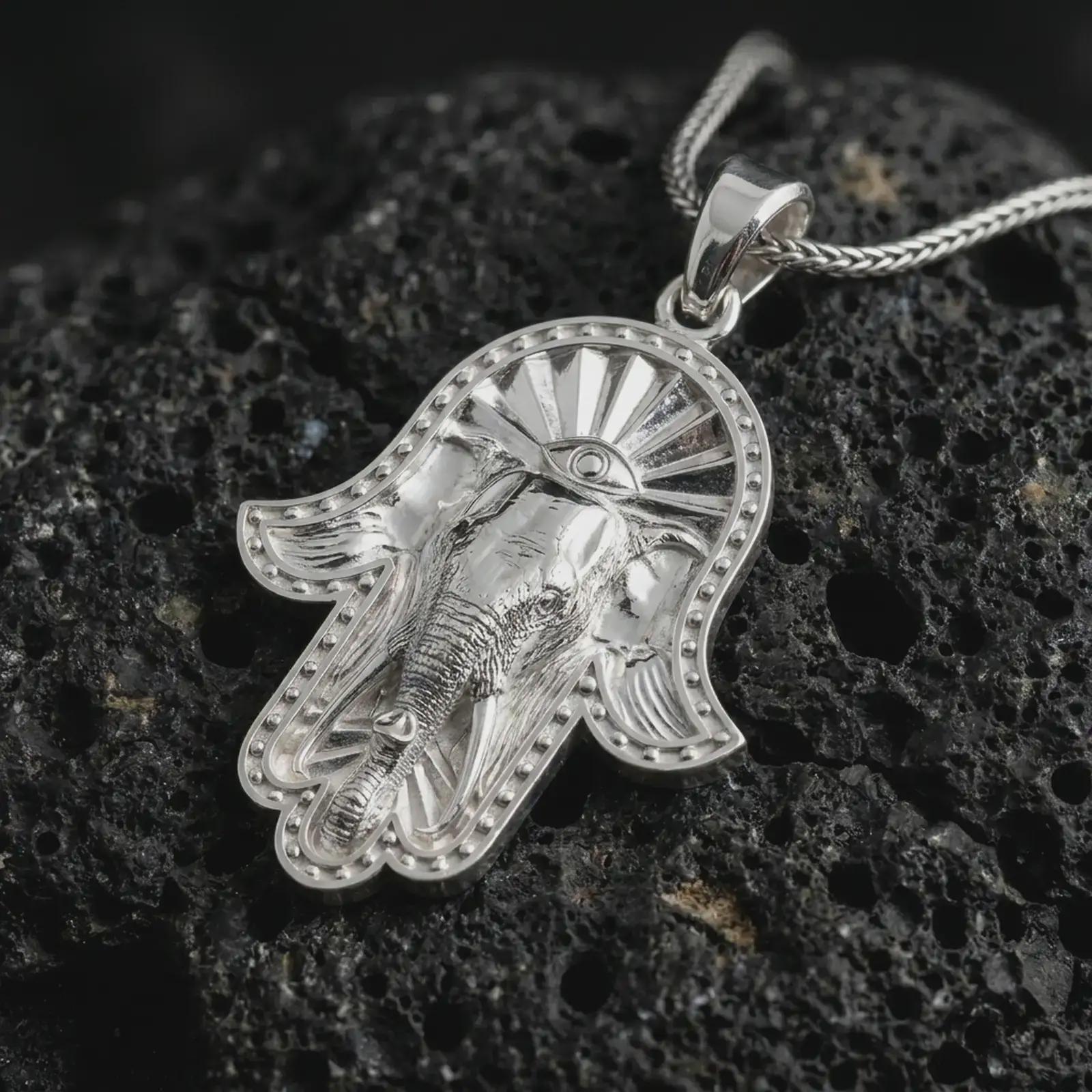 Polished silver hamsa elephant pendant necklace on textured volcanic rock, centered macro jewelry photo with detailed elephant trunk, tusks, spiritual eye motif, and bright silver highlights.