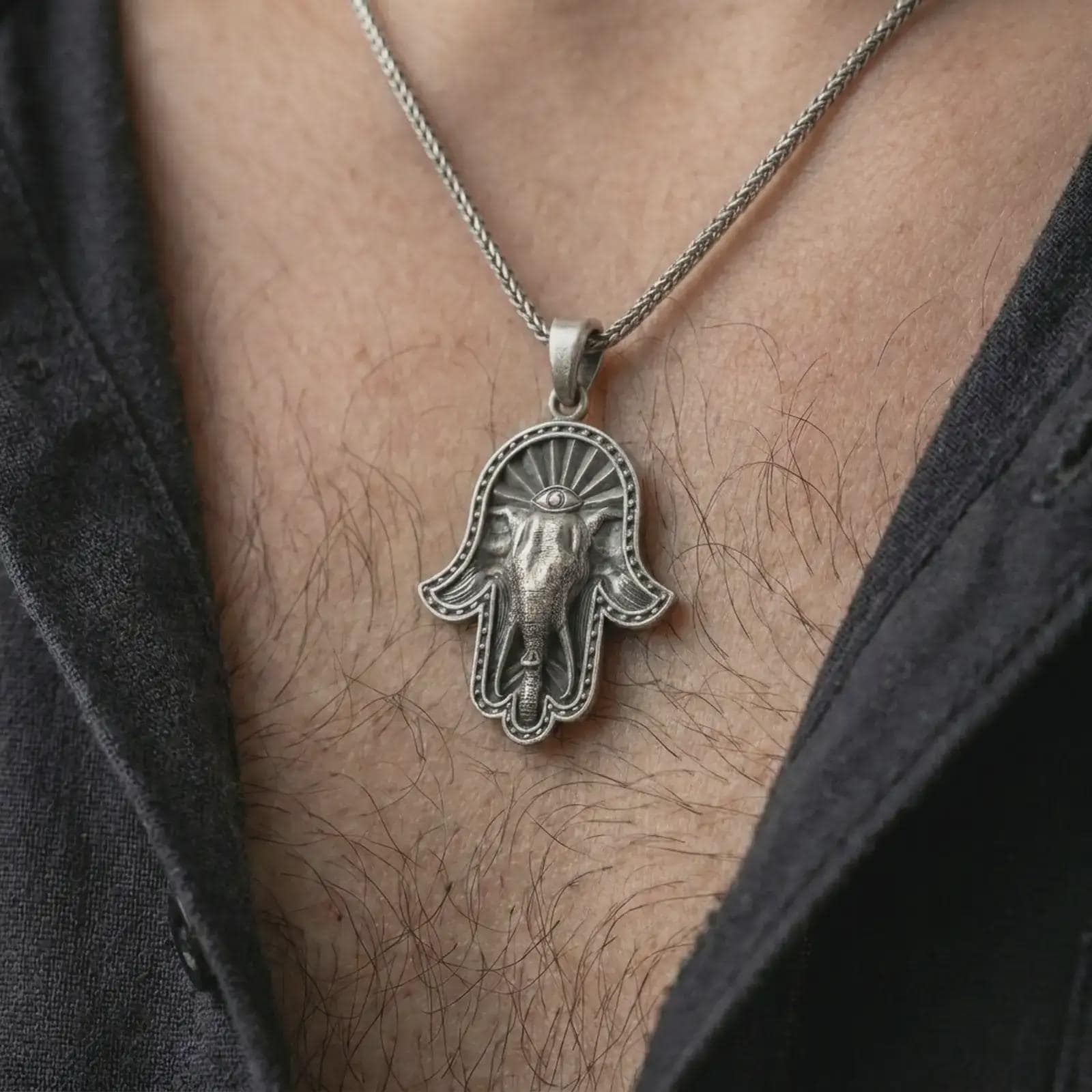 Oxidized hamsa elephant pendant necklace worn on the chest, close-up lifestyle jewelry photo showing the protective elephant amulet on a spiga chain with dark clothing.