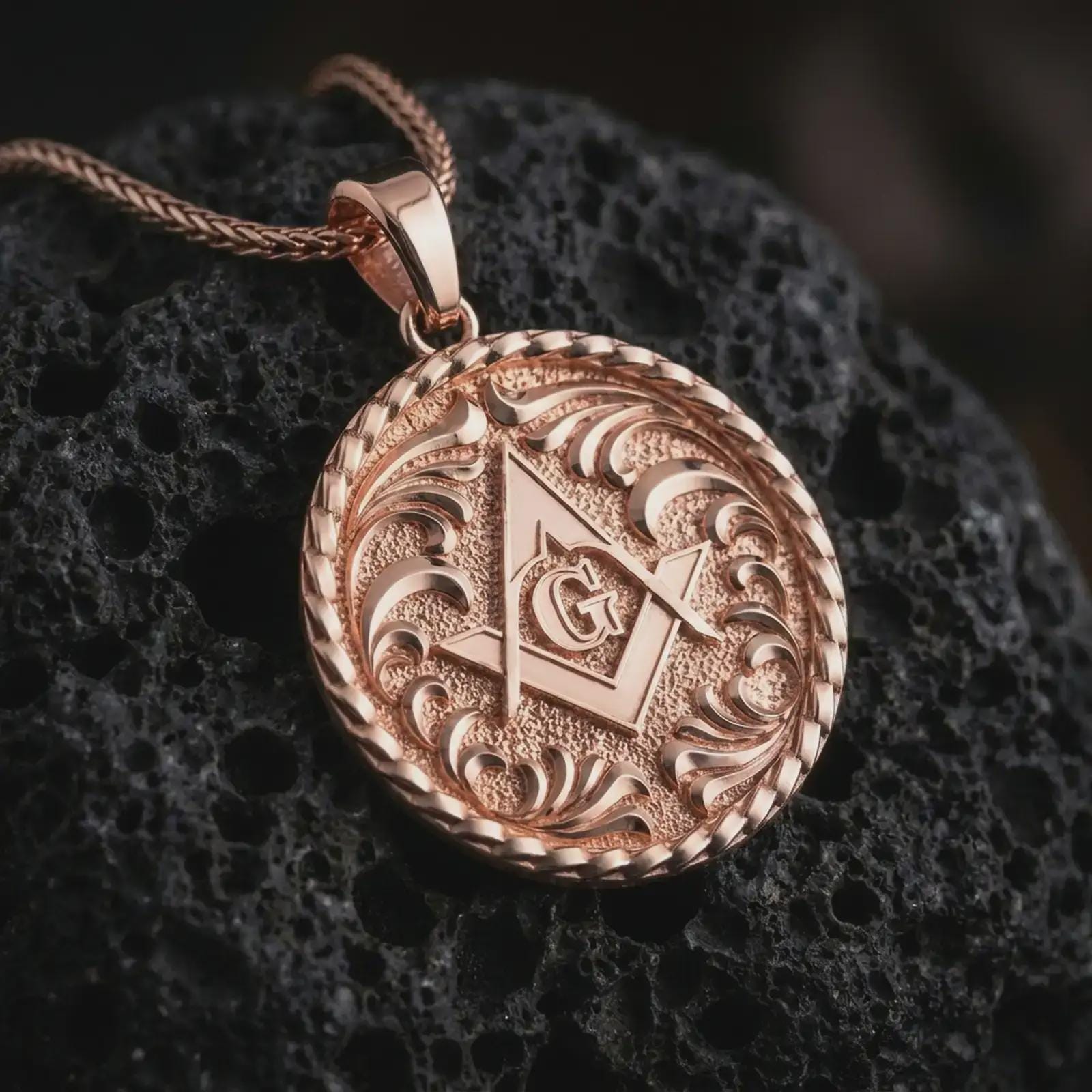 Rose gold plated Masonic pendant necklace on textured volcanic rock, detailed macro product shot with soft warm reflections and symbolic Freemason styling.