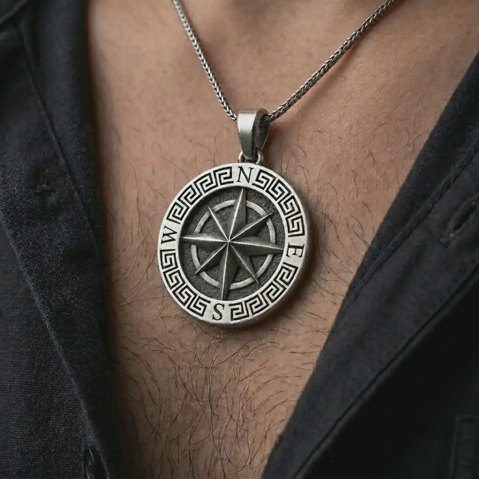 Oxidized Greek compass pendant necklace worn on the chest, close-up lifestyle jewelry photo showing the navigation medallion on a spiga chain with dark clothing.
