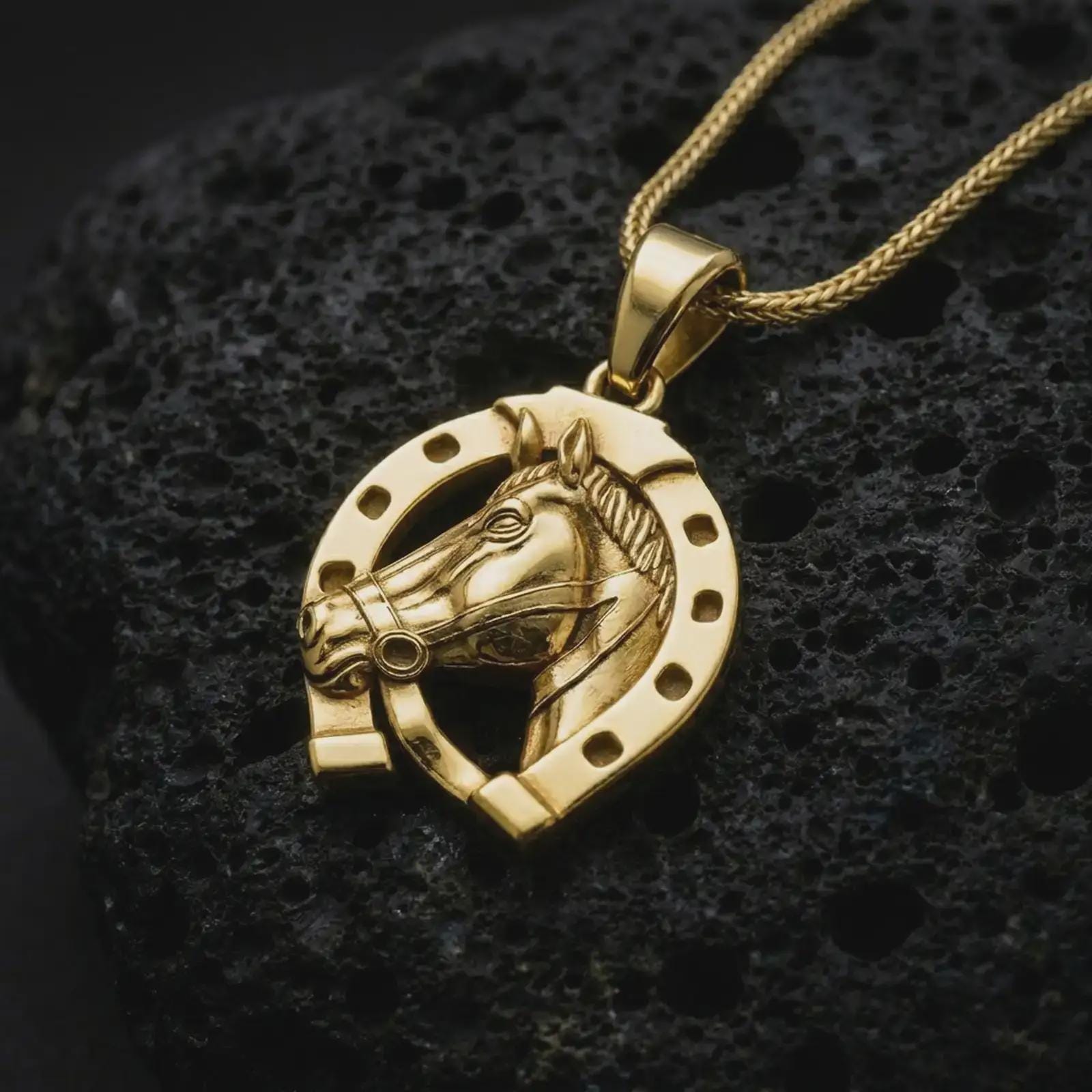 Gold plated horseshoe pendant necklace on textured volcanic rock, premium close-up studio composition emphasizing the good luck symbol, horse head detail, and protective charm design.