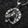 Load image into Gallery viewer, Oxidized horseshoe pendant necklace on textured volcanic rock, close-up studio shot highlighting the horse head relief, lucky horseshoe frame, openwork design, and antique silver contrast.
