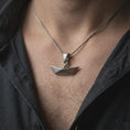 Load image into Gallery viewer, Oxidized origami boat pendant necklace worn on the chest, close-up lifestyle jewelry photo showing the geometric boat charm on a spiga chain with dark clothing.
