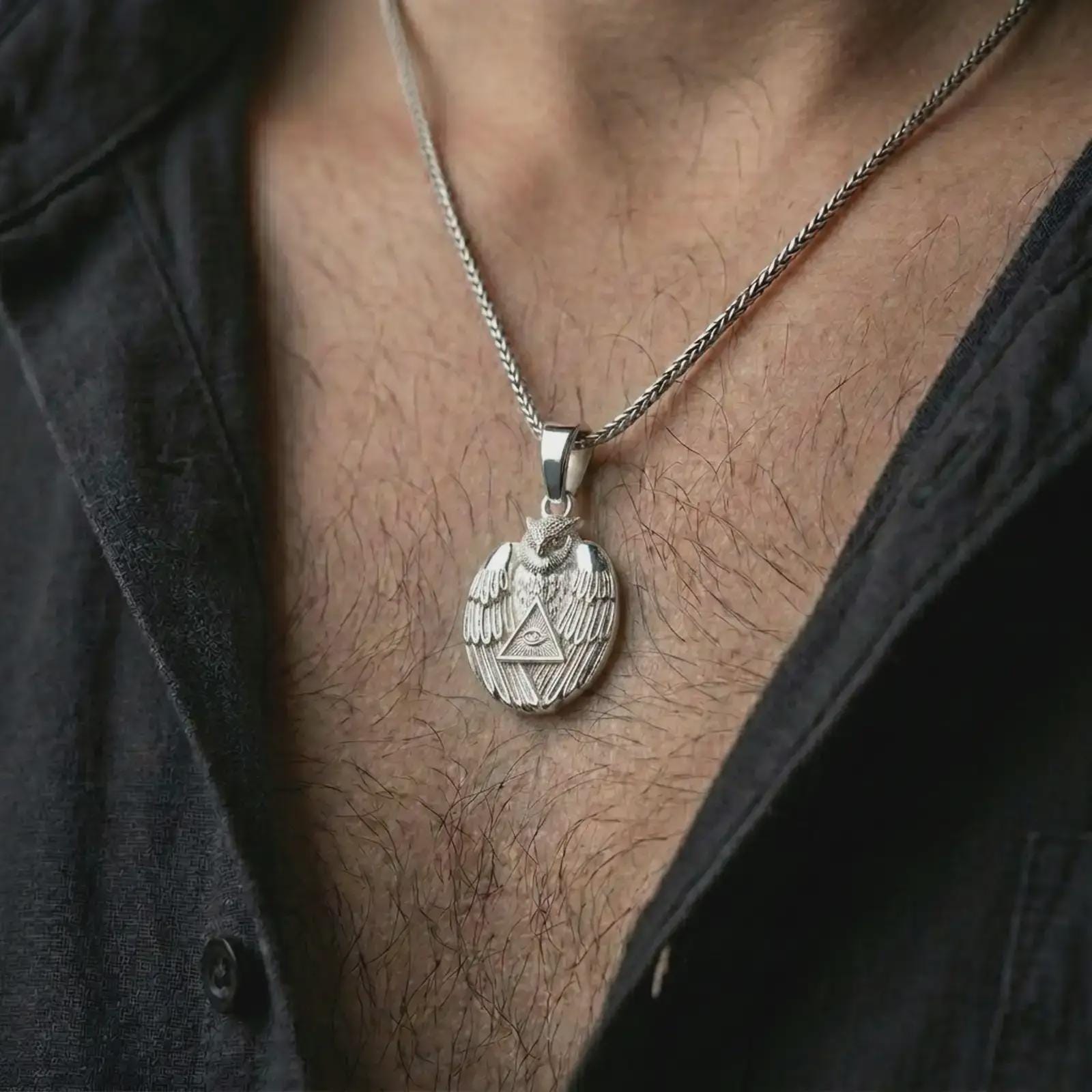 Polished silver owl all-seeing eye pendant necklace worn on the chest, masculine lifestyle shot highlighting the bright silver finish, feathered wings, and triangle eye detail.