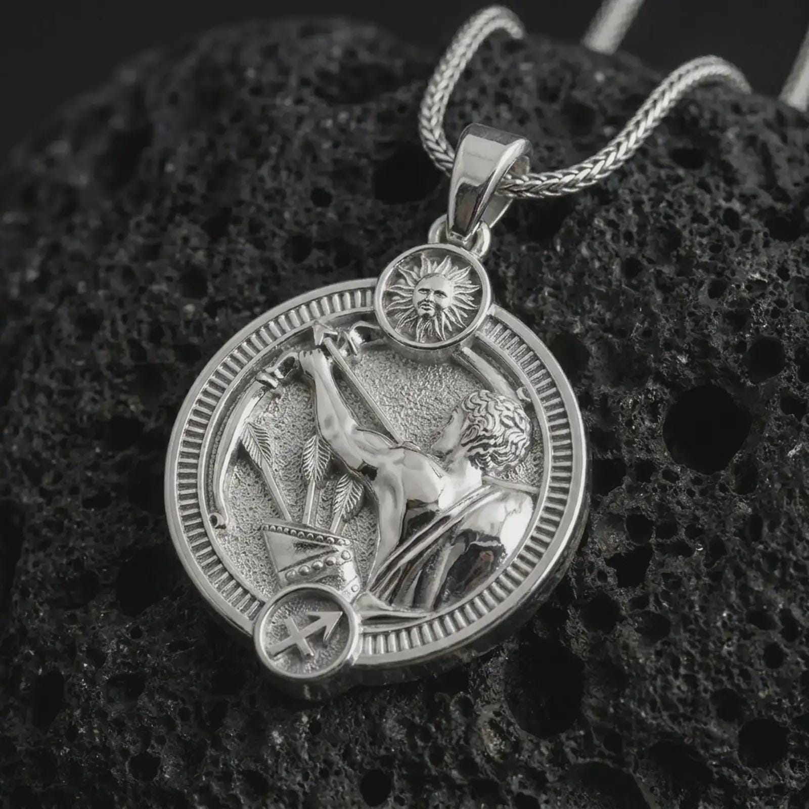 Polished silver Sagittarius zodiac pendant necklace on textured volcanic rock, centered macro jewelry photo with detailed archer horoscope relief and bright silver highlights.