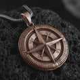 Load image into Gallery viewer, Bronze compass pendant necklace on textured volcanic rock, close-up studio shot highlighting the raised compass rose, directional letters, ridged outer border, and antique silver contrast.
