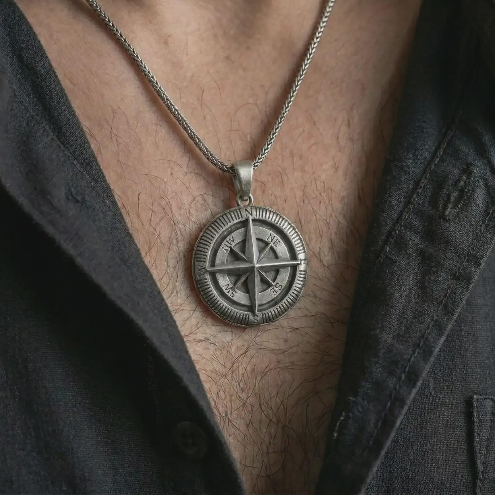 Oxidized compass pendant necklace worn on the chest, close-up lifestyle jewelry photo showing the nautical navigation medallion on a spiga chain with dark clothing.