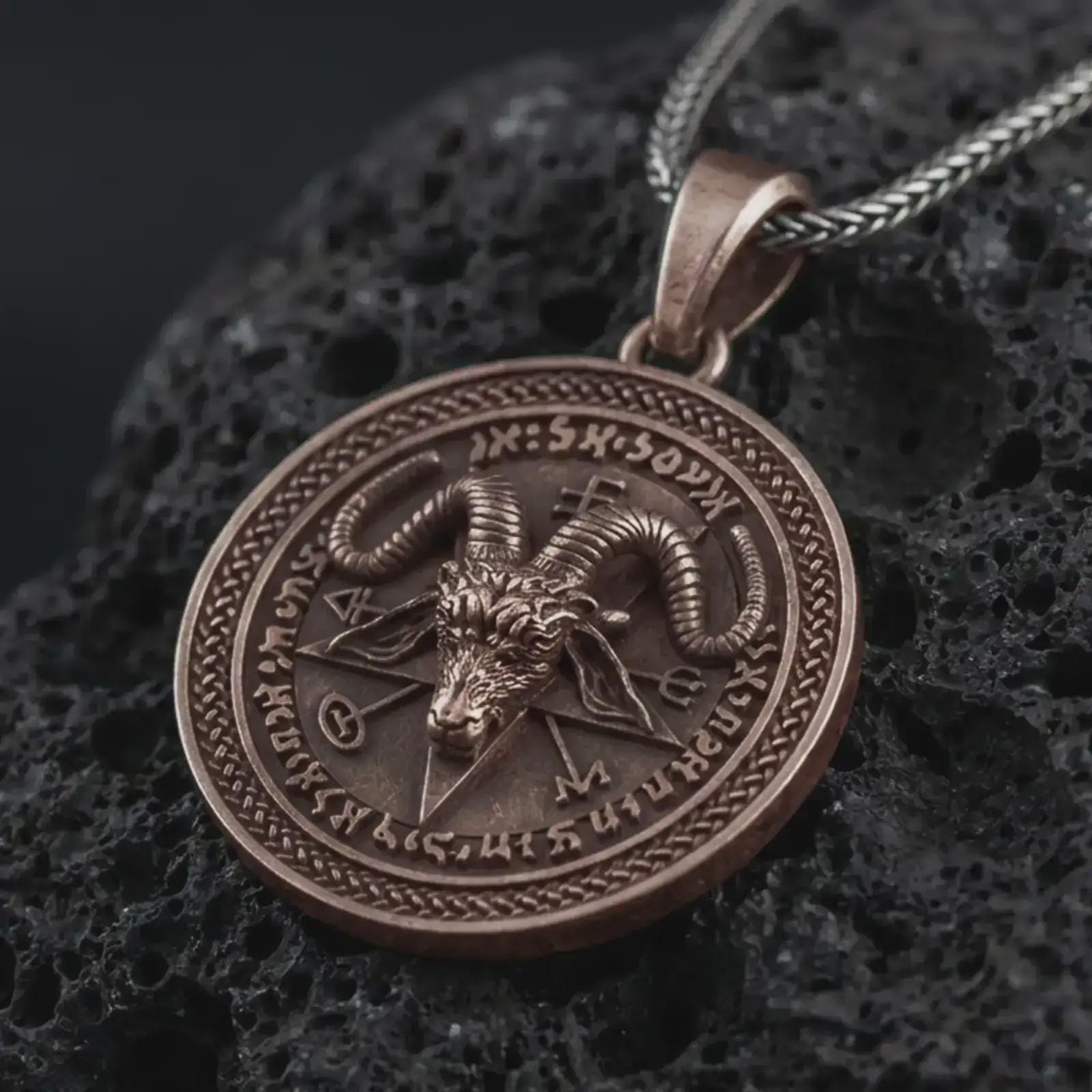 Bronze Baphomet pendant necklace on textured volcanic rock, close-up studio shot highlighting the goat head relief, pentagram background, occult sigils, and antique silver contrast.
