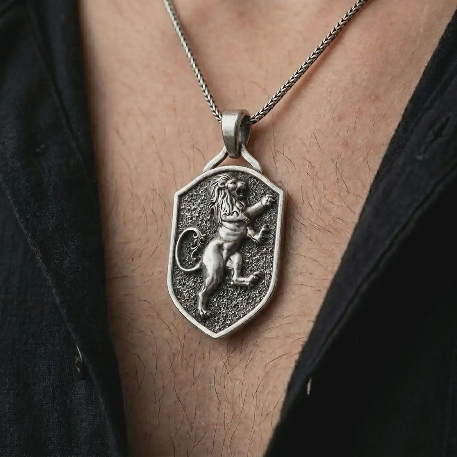 Oxidized heraldic lion shield pendant necklace worn on the chest, close-up lifestyle jewelry photo showing the medieval lion crest on a spiga chain with dark clothing.