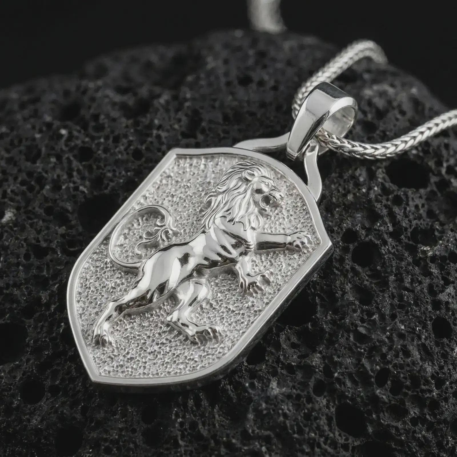 Polished silver heraldic lion shield pendant necklace on textured volcanic rock, centered macro jewelry photo with detailed lion mane, raised paws, and bright silver highlights.