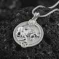 Load image into Gallery viewer, Polished silver Taurus zodiac pendant necklace on textured volcanic rock, centered macro jewelry photo with detailed bull horoscope relief and bright silver highlights.
