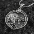 Load image into Gallery viewer, Oxidized Taurus zodiac pendant necklace on textured volcanic rock, close-up studio shot highlighting the bull relief, sun detail, Taurus symbol, and antique silver contrast.
