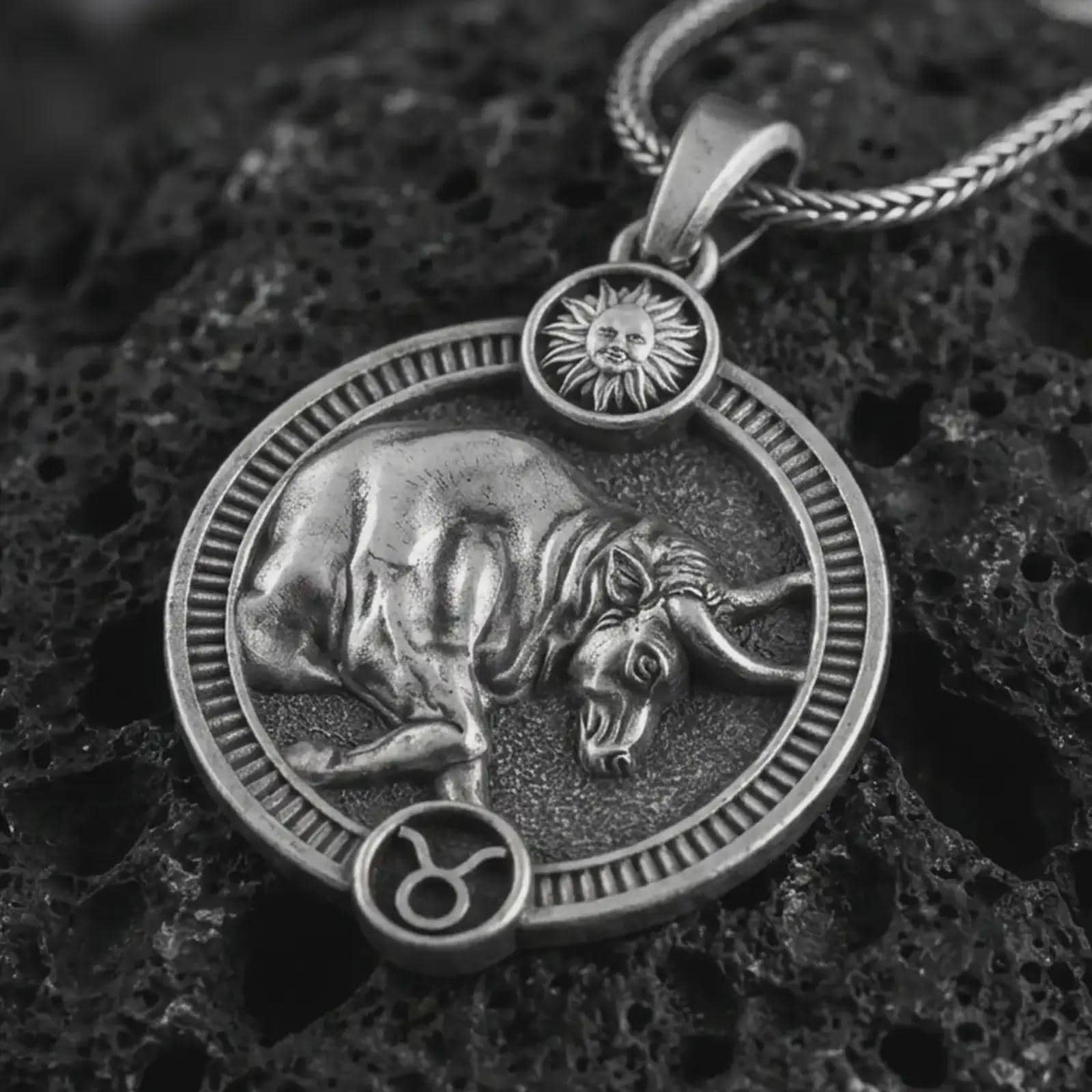 Oxidized Taurus zodiac pendant necklace on textured volcanic rock, close-up studio shot highlighting the bull relief, sun detail, Taurus symbol, and antique silver contrast.