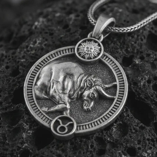 Oxidized Taurus zodiac pendant necklace on textured volcanic rock, close-up studio shot highlighting the bull relief, sun detail, Taurus symbol, and antique silver contrast.
