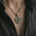 Load image into Gallery viewer, Oxidized Capricorn zodiac pendant necklace worn on the chest, close-up lifestyle jewelry photo showing the sea goat astrology medallion on a spiga chain with dark clothing.
