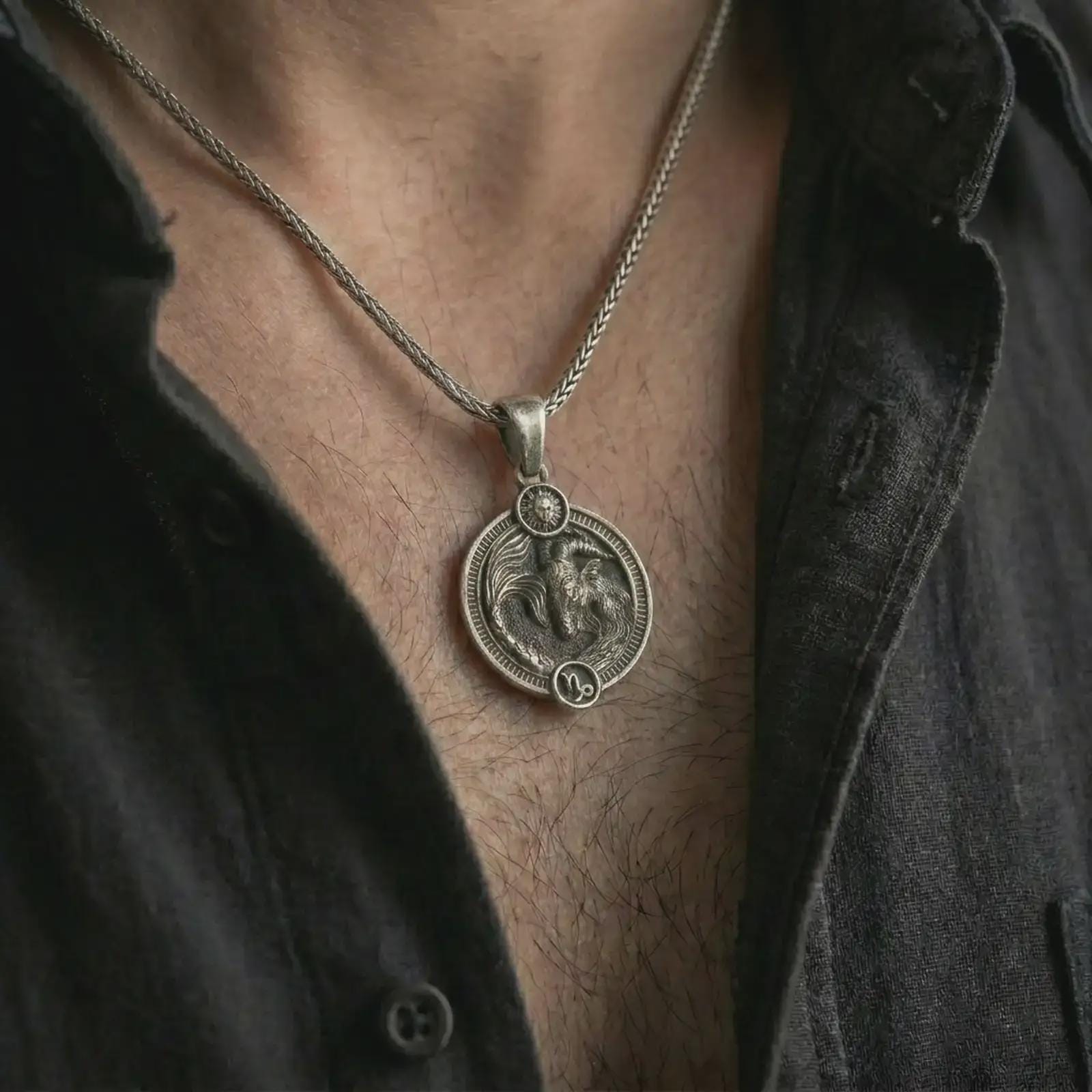 Oxidized Capricorn zodiac pendant necklace worn on the chest, close-up lifestyle jewelry photo showing the sea goat astrology medallion on a spiga chain with dark clothing.
