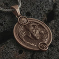 Load image into Gallery viewer, Bronze Capricorn zodiac pendant necklace on textured volcanic rock, close-up studio shot highlighting the sea goat relief, sun detail, Capricorn symbol, and antique silver contrast.
