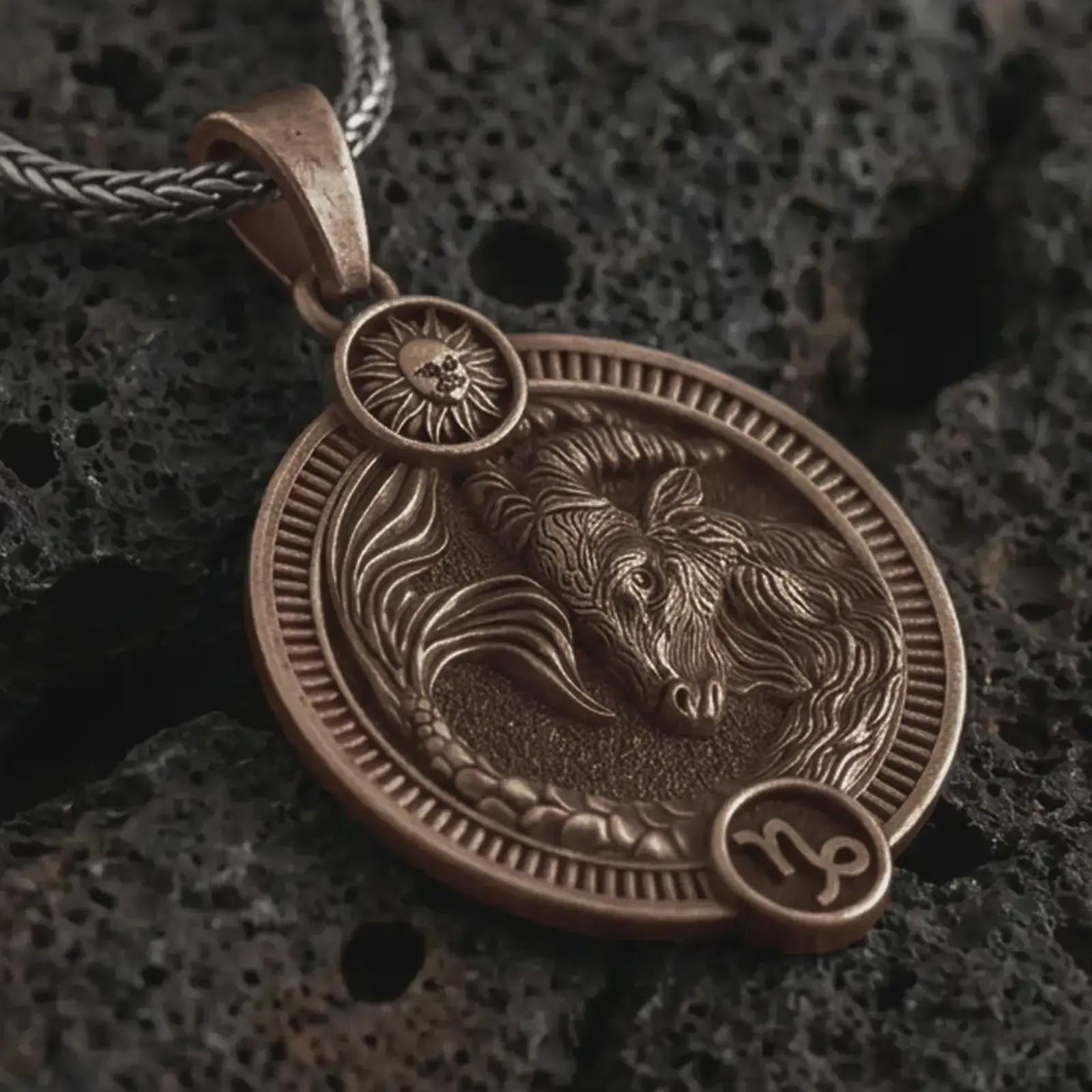 Bronze Capricorn zodiac pendant necklace on textured volcanic rock, close-up studio shot highlighting the sea goat relief, sun detail, Capricorn symbol, and antique silver contrast.