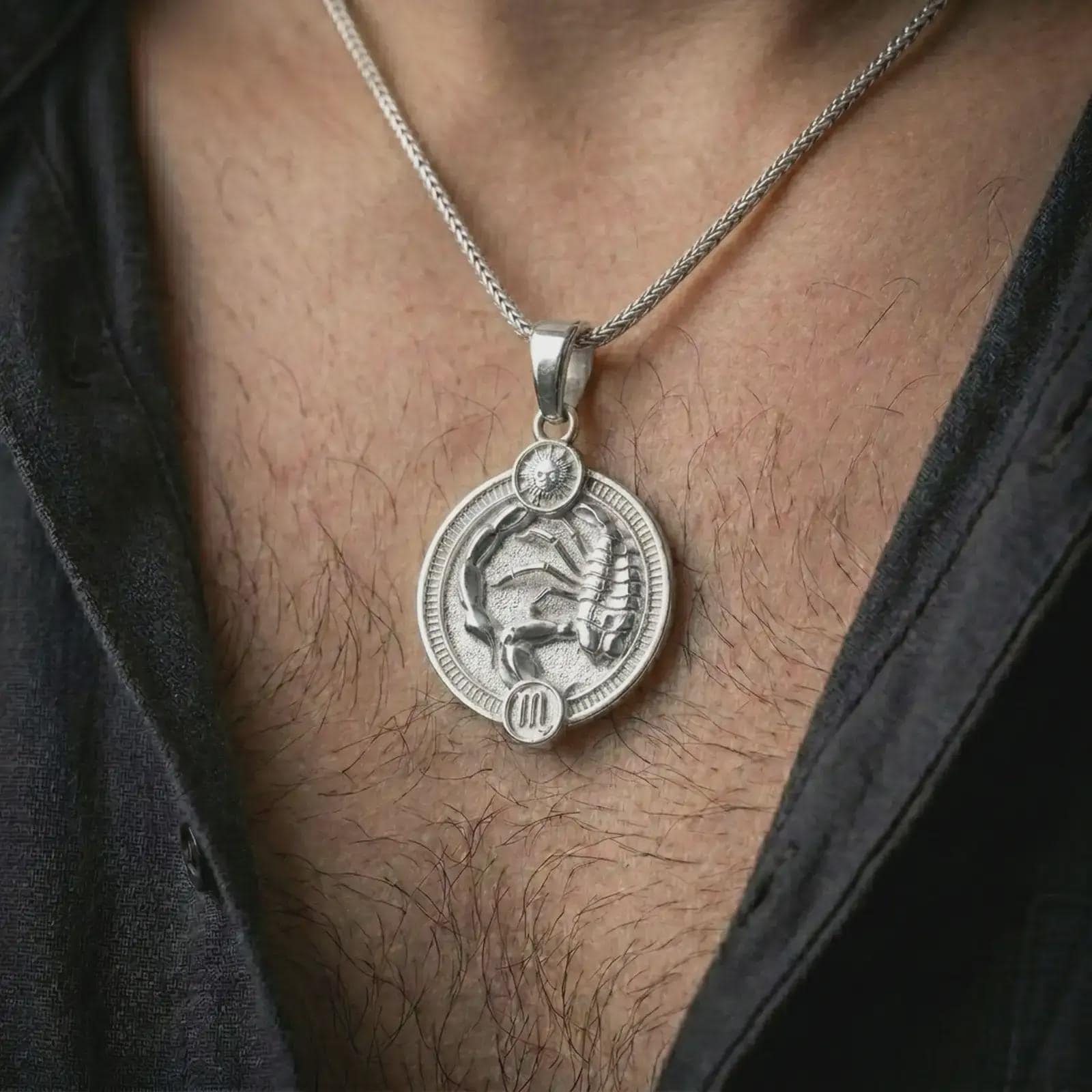 Polished silver Scorpio zodiac pendant necklace worn on the chest, masculine lifestyle shot highlighting the scorpion relief, sun detail, and bright silver finish.