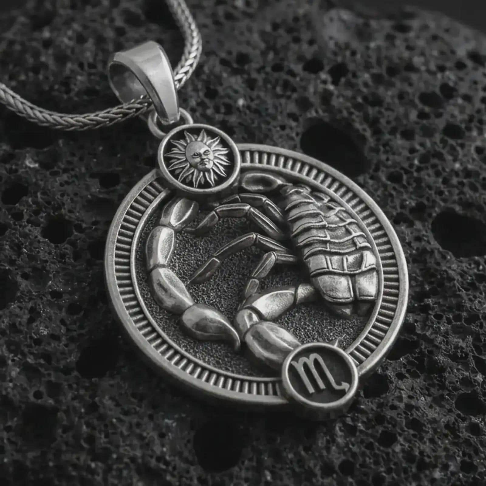 Oxidized Scorpio zodiac pendant necklace on textured volcanic rock, close-up studio shot highlighting the scorpion relief, sun detail, Scorpio symbol, and antique silver contrast.