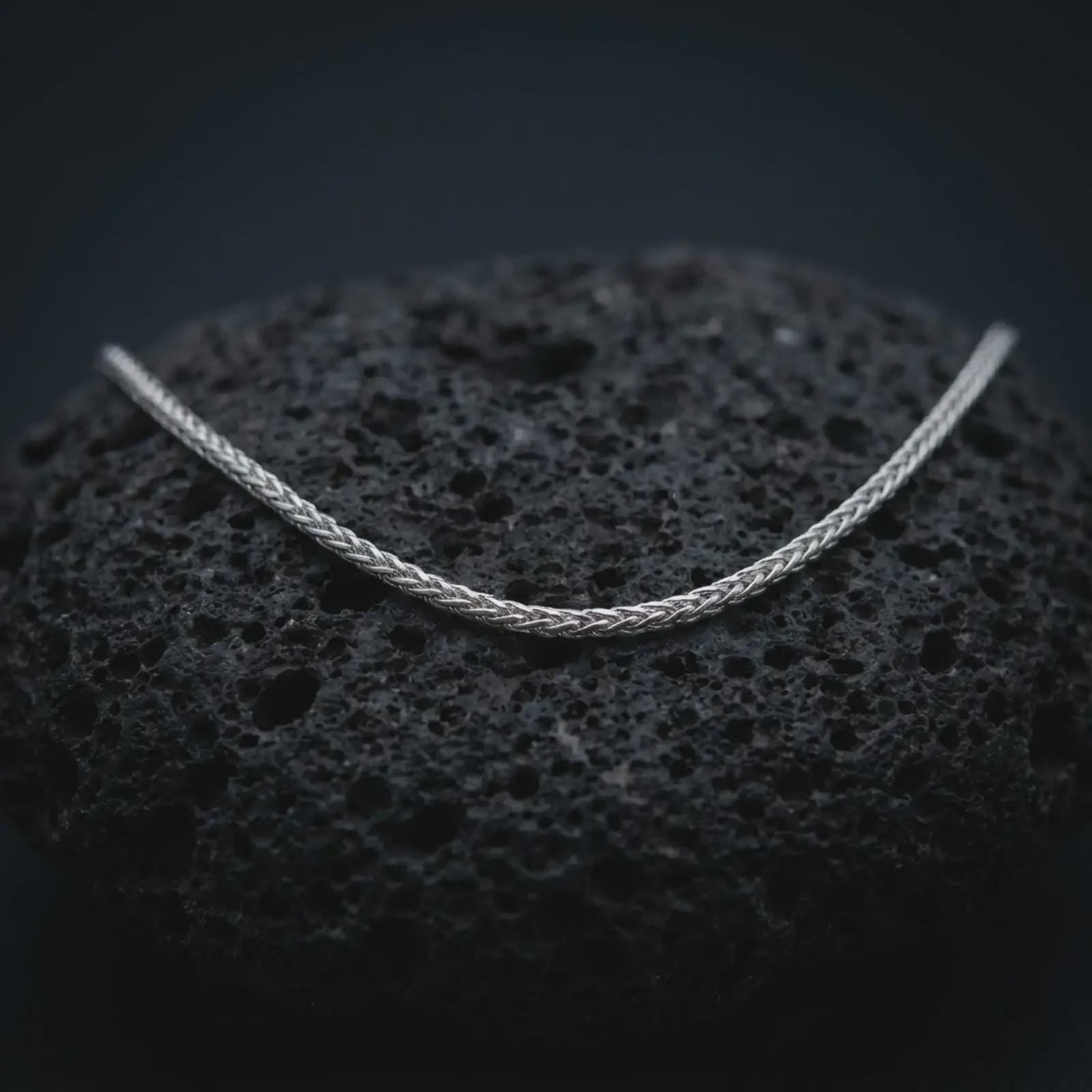 A polished silver foxtail chain necklace is displayed on black volcanic rock in a premium macro studio close-up with sharp Italian wheat chain detail.