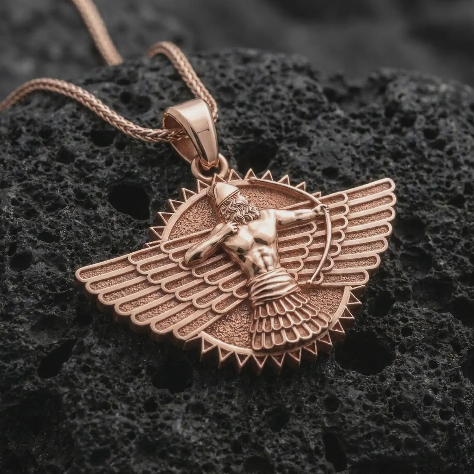 A rose gold plated Faravahar pendant is photographed on porous volcanic rock in a close-up studio composition with refined luxury lighting and historical detail.