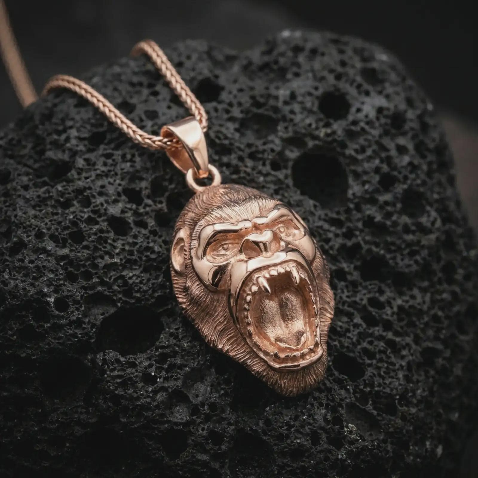 A rose gold plated gorilla pendant is photographed on porous volcanic rock in a close-up studio composition with refined luxury lighting and sculpted fur detail.