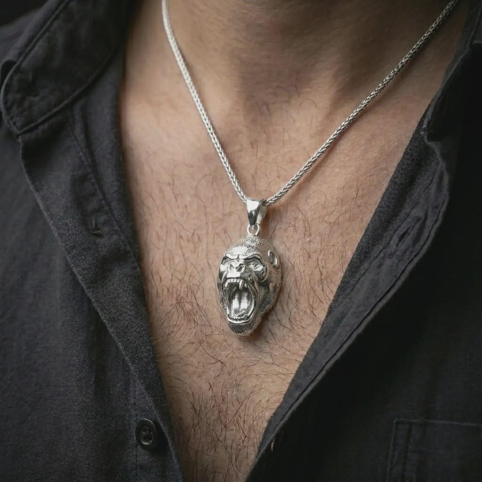 A polished silver gorilla pendant is worn on the neck in a premium close-up lifestyle image, showing the roaring ape face clearly.