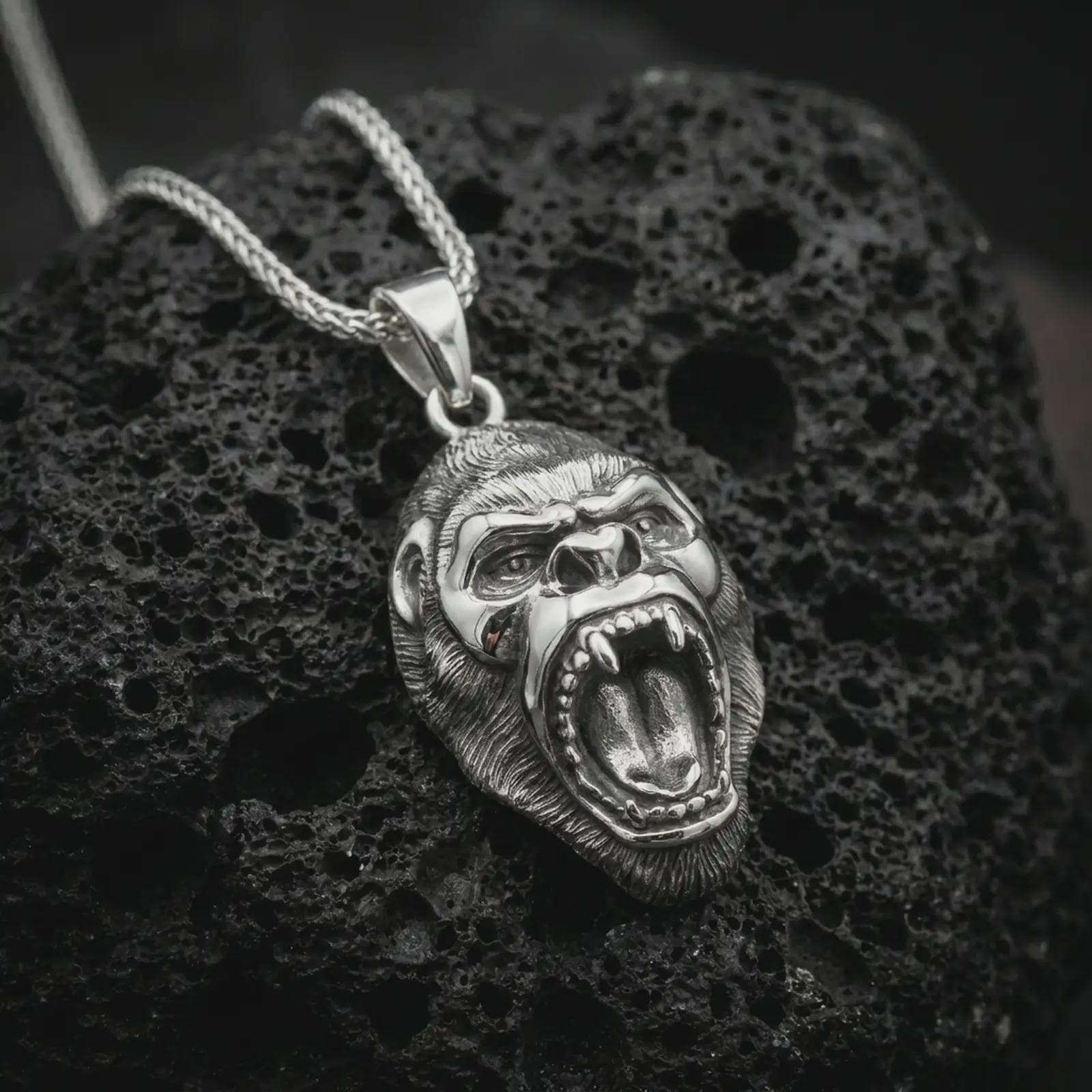 A polished silver gorilla pendant is displayed on black volcanic rock in a premium macro studio close-up with sharp facial detail and bold animal character.