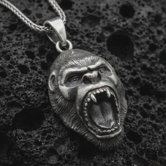 An oxidized gorilla pendant rests on dark volcanic rock in a macro studio close-up, showing a fierce roaring ape head with detailed teeth and fur texture.