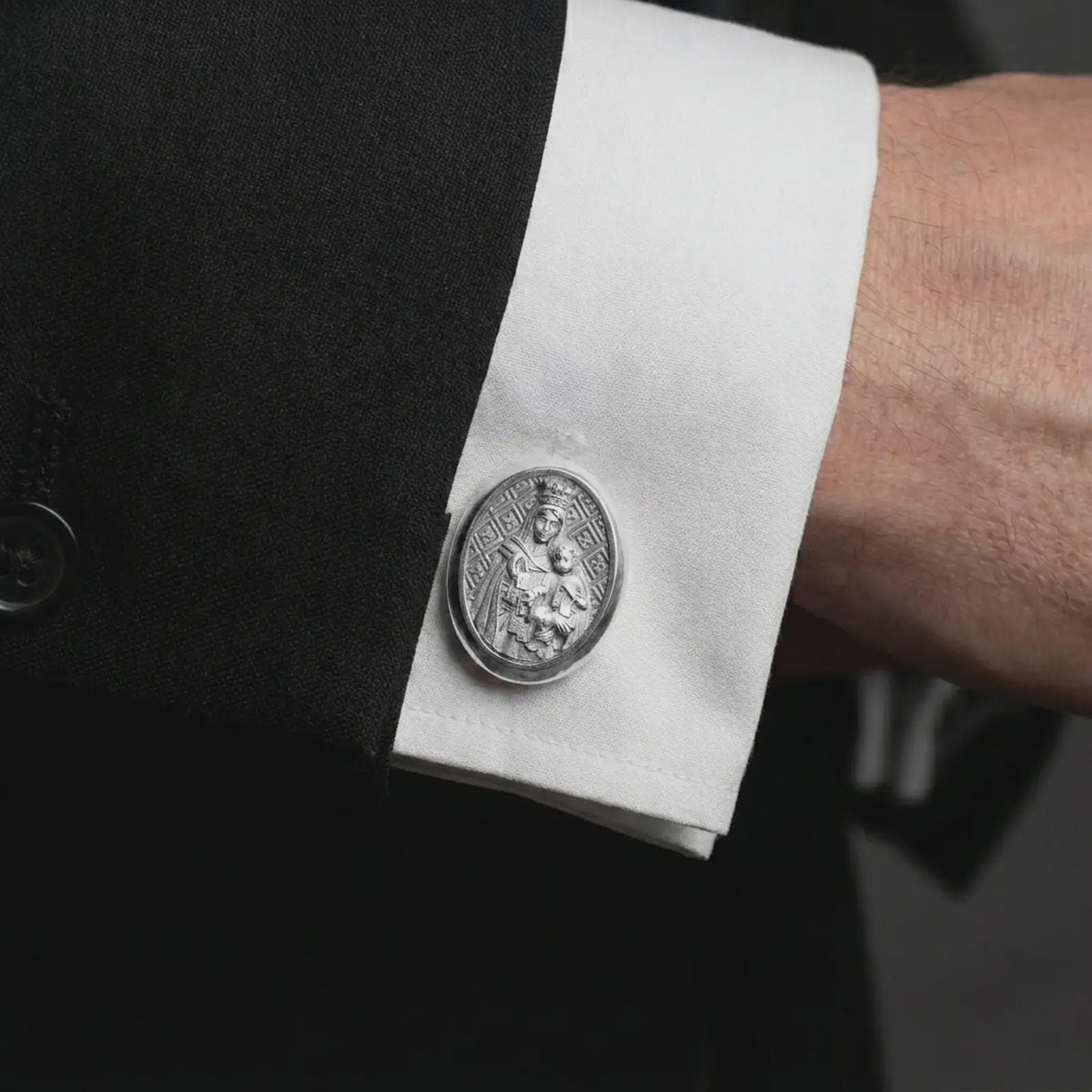 A polished silver Blessed Mother cufflink is worn on a shirt cuff in a premium close-up lifestyle image, showing the Virgin Mary and Child relief clearly.