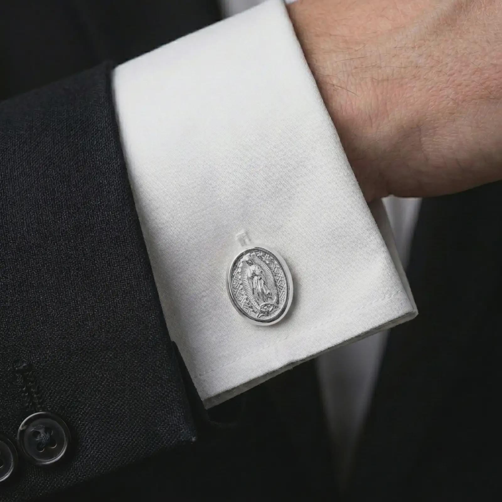 A polished silver Our Lady of Guadalupe cufflink is worn on a shirt cuff in a premium close-up lifestyle image, showing the sacred Virgin Mary relief clearly.
