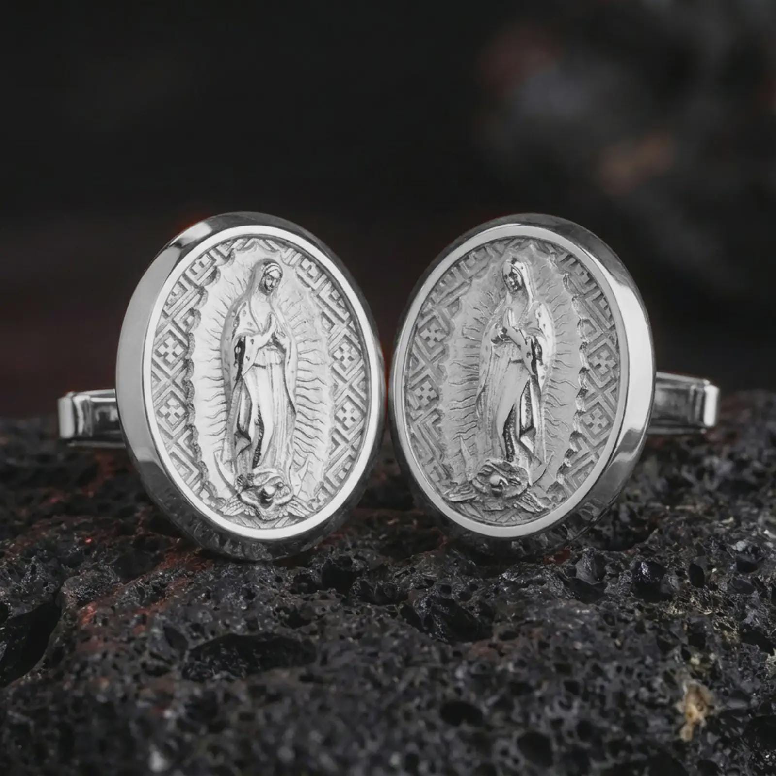 Polished silver Our Lady of Guadalupe cufflinks are displayed on black volcanic rock in a premium macro studio close-up with detailed Catholic devotional artwork.