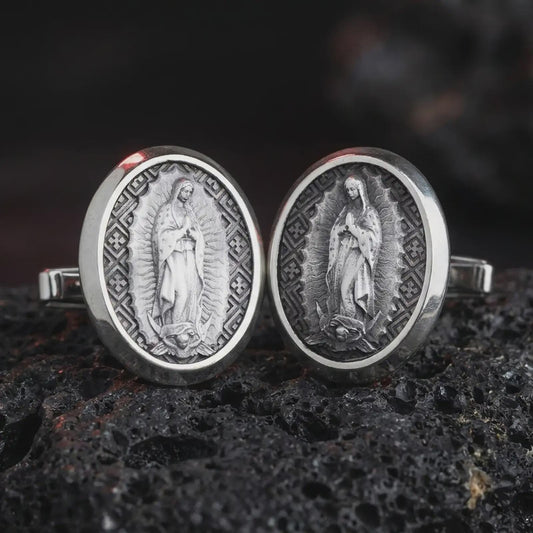 An oxidized Our Lady of Guadalupe cufflink pair rests on dark volcanic rock in a macro studio close-up, showing the Virgin Mary relief in oval frames.