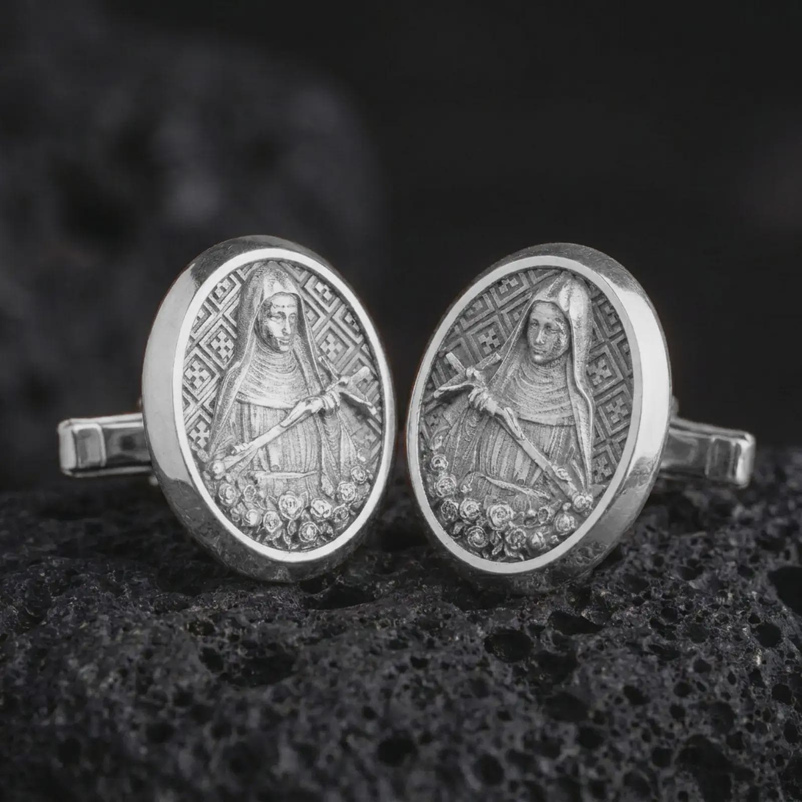 Polished silver Mary Magdalene cufflinks are displayed on black volcanic rock in a premium macro studio close-up with detailed Christian devotional artwork.