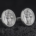 Load image into Gallery viewer, An oxidized St Dominic cufflink pair rests on dark volcanic rock in a macro studio close-up, showing a detailed Catholic saint relief inside oval frames.
